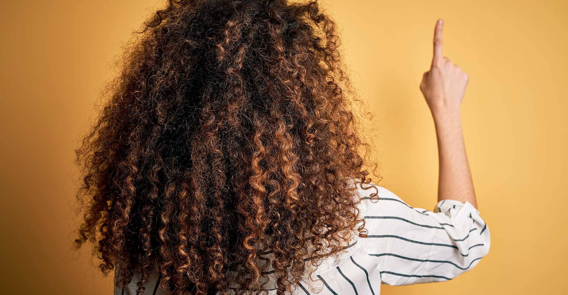 Mulher de costas cacheada com algumas madeixas mais claras